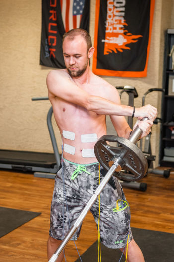 Athlete performing landmine rotation exercise with electrical stimulation pads on core to improve strength and movment efficiency using Phoenix Waveform