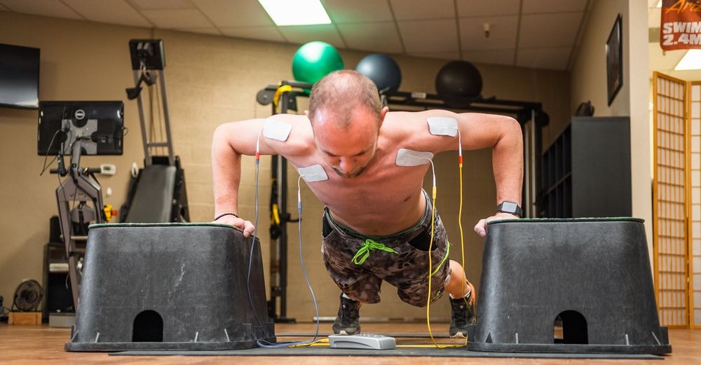 athlete doing isometric pushup with electrode pads on chest and shoulder activating the muscles with direct current neurotherapy Phoenix Waveform